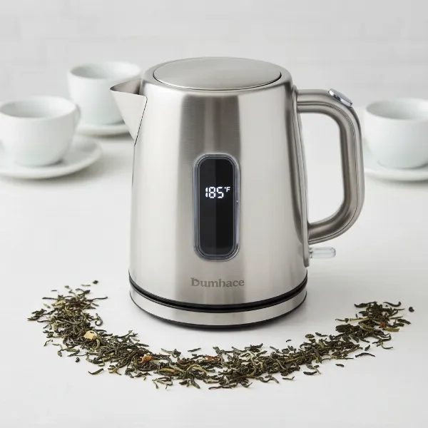 A sleek stainless steel variable temperature kettle with digital display and tea leaves.